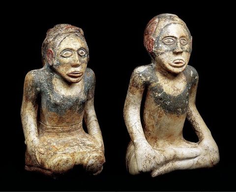 Sculpture. Two statuettes of a woman kneeling on her shins and a man sitting with legs crossed. Both lean their torsos forward and look ahead, eyes wide open and lips parted. Traces of dark and red paint are visible.